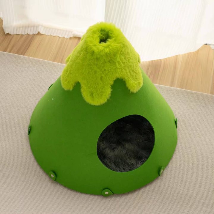 Green felt cone-shaped cat house with a plush textured peak, shown on a rug in a room setting.