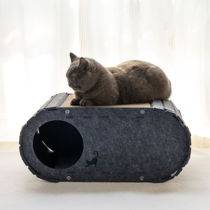 Dark grey felt capsule-shaped cat tunnel bed with a corrugated cardboard top pad and a round side entrance, shown with a cat resting on top.