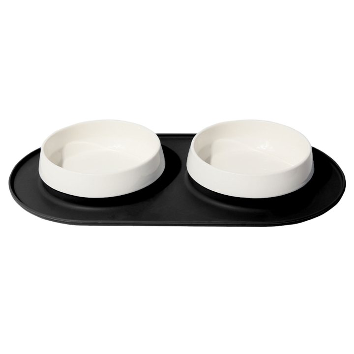 Two white ceramic pet bowls set into an oval black silicone mat