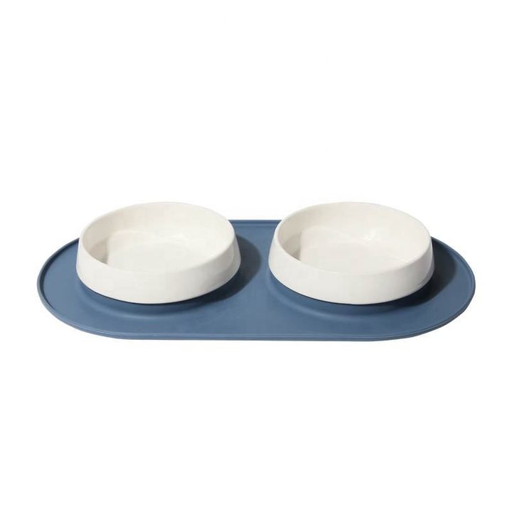 Two white ceramic pet bowls set into an oval blue-grey silicone mat