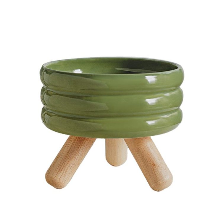 Olive-green ribbed ceramic pet bowl standing on wooden tripod legs