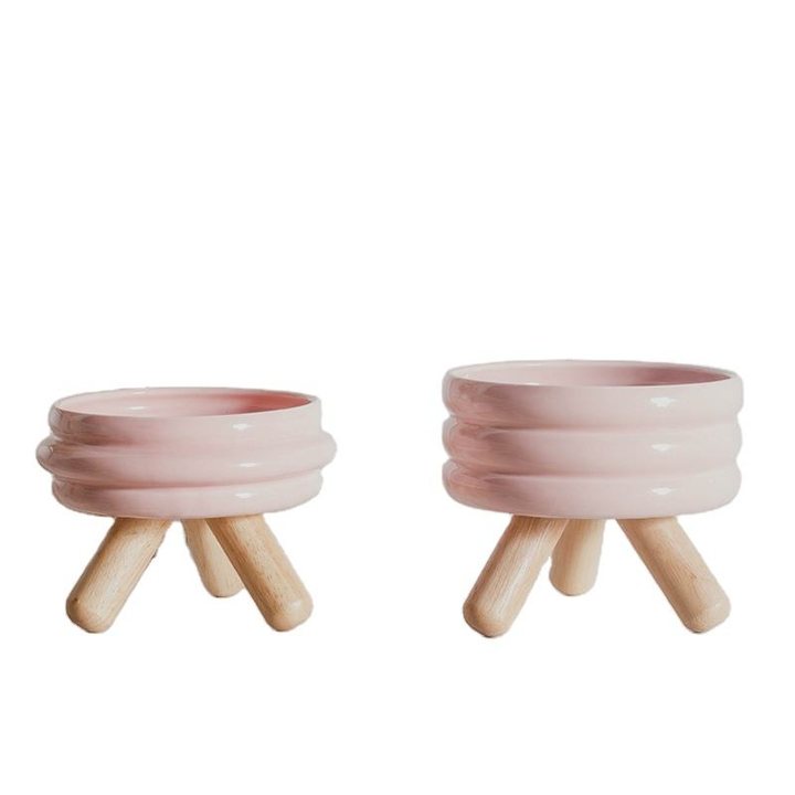 Pink ribbed ceramic pet bowls of two sizes, standing on wooden tripod legs
