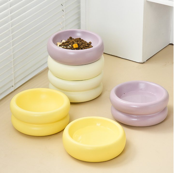 Small footed ceramic pet bowls in lavender, cream, and pale yellow, shown in a home setting