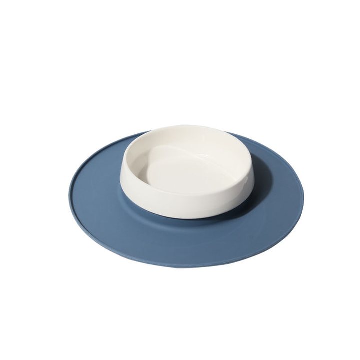 White ceramic pet bowl set on a round blue-grey silicone mat.