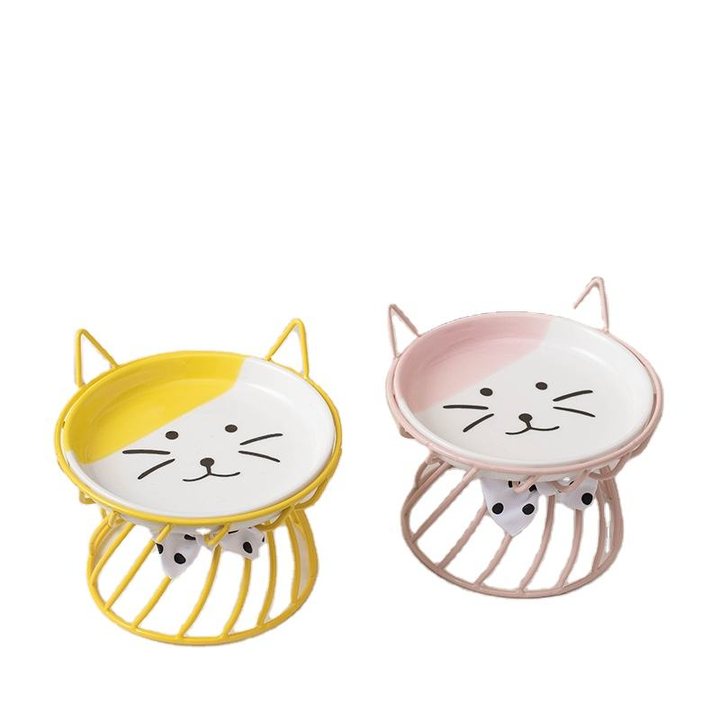 Two cat-face ceramic dishes, in yellow and pink, each set in a round wire stand with a bow-tie accent.