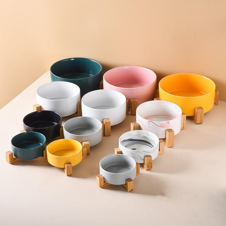 Assorted ceramic pet bowls in different sizes and colours, each resting in its own wooden cradle stand.