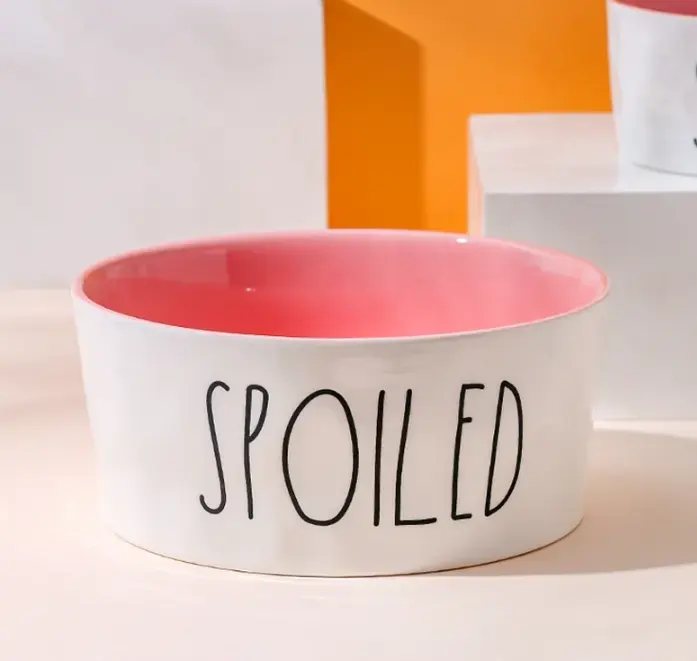 White ceramic pet bowl with a coral-pink glazed interior and a printed slogan on the outside.