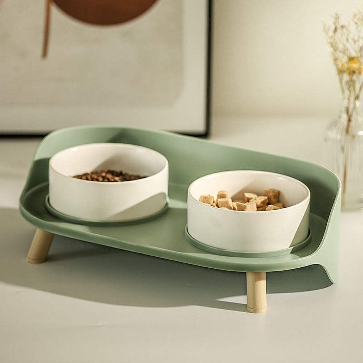 Sage-green pet feeding tray on short wooden legs, holding two white ceramic bowls.