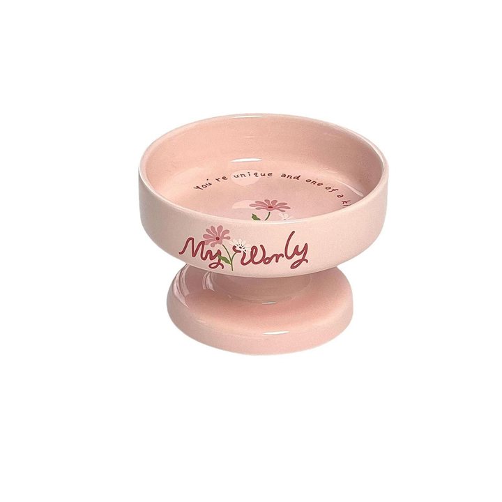Footed pink ceramic cat bowl on a pedestal base, printed with a small floral design and slogan.