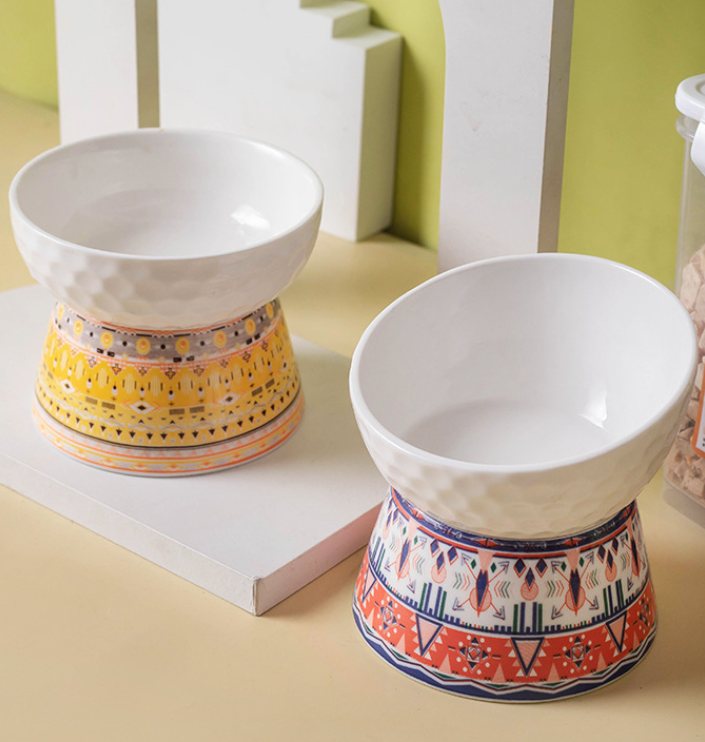 Two footed ceramic pet bowls with a colourful folk-pattern border printed on the pedestal base.