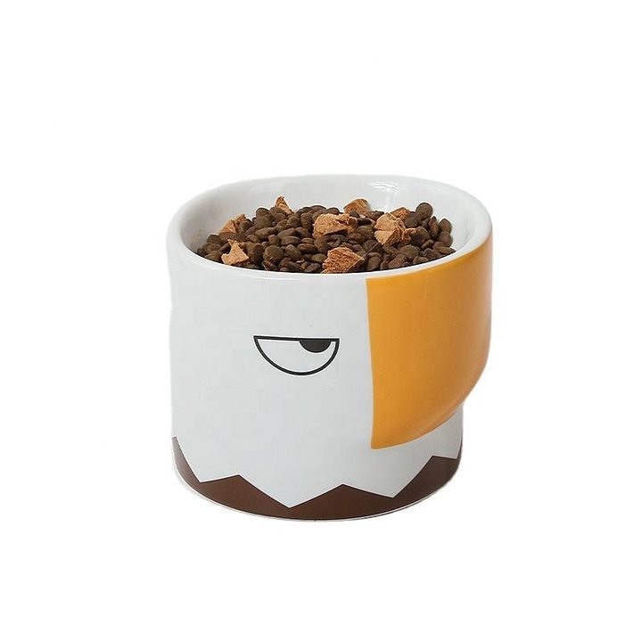 Ceramic pet bowl shaped like an owl's face, filled with dry kibble.