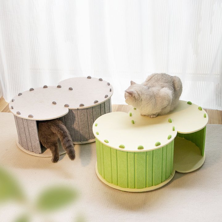 Two colorways of a twin-chamber felt cat house in a bright room with cats climbing on and inside them.