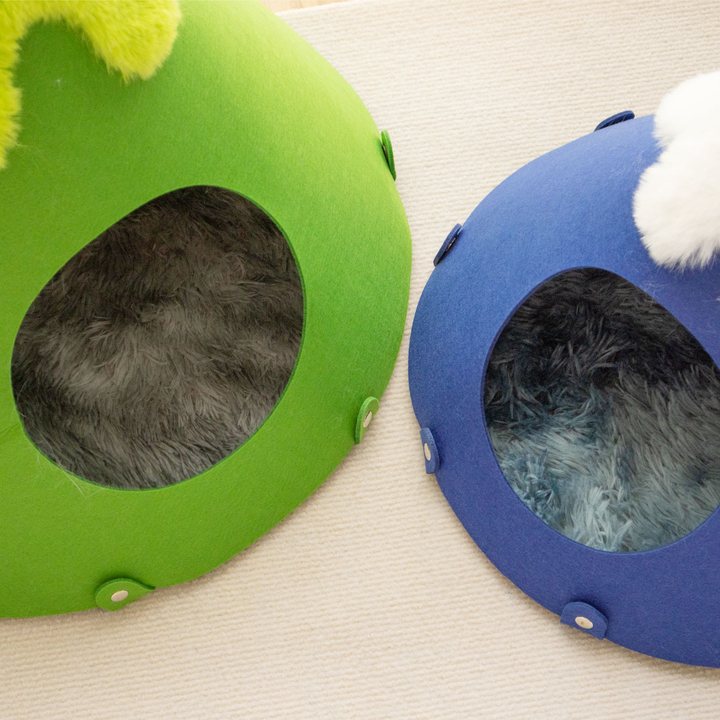Two mountain-shaped felt cat caves, green and blue, each with a plush contrast-color summit, viewed from above.