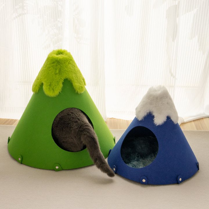 Two mountain-shaped felt cat caves in green and blue in a bright room, with a cat's tail visible entering one.