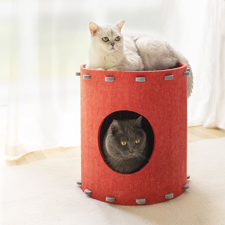 Cylindrical red felt cat house with a pull-tab lid, one cat resting on top and another peeking from the entrance.