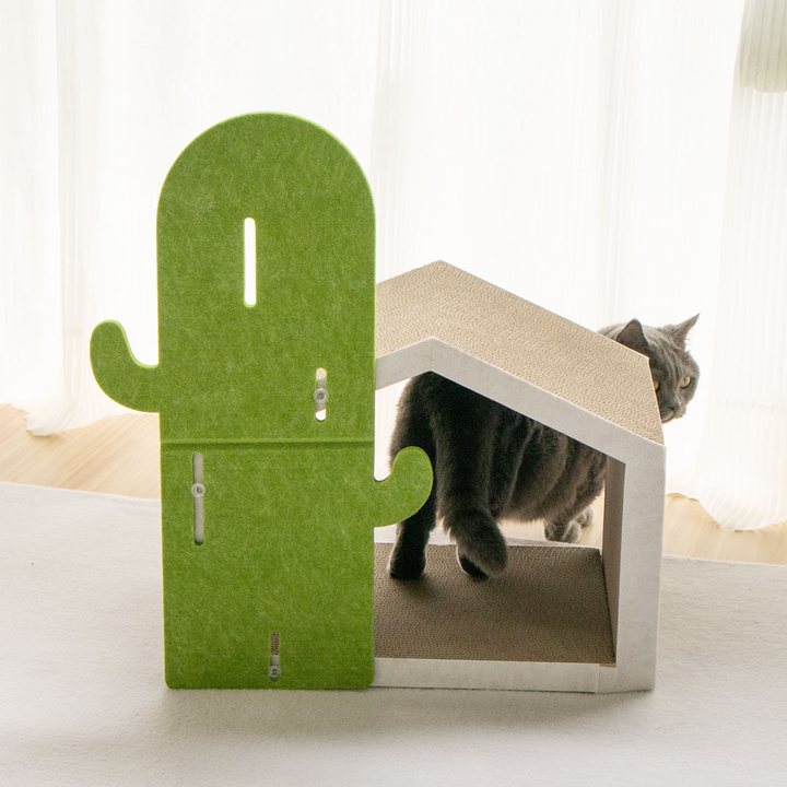 Green felt cactus-shaped scratching panel standing beside a beige corrugated cardboard peaked cat house with a scratch-pad roof