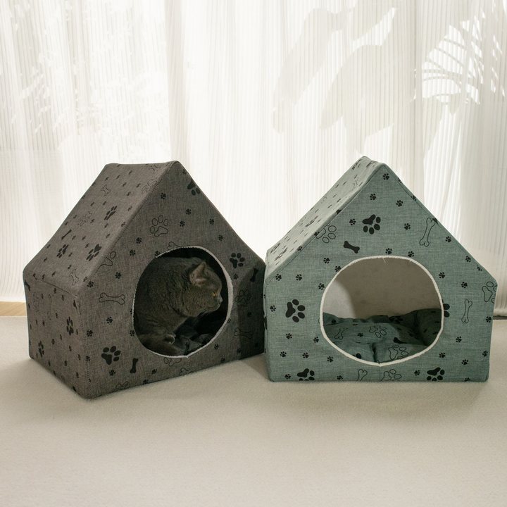 Two peaked fabric cat houses printed with a paw-and-bone pattern, one dark gray and one sage green, round doorway