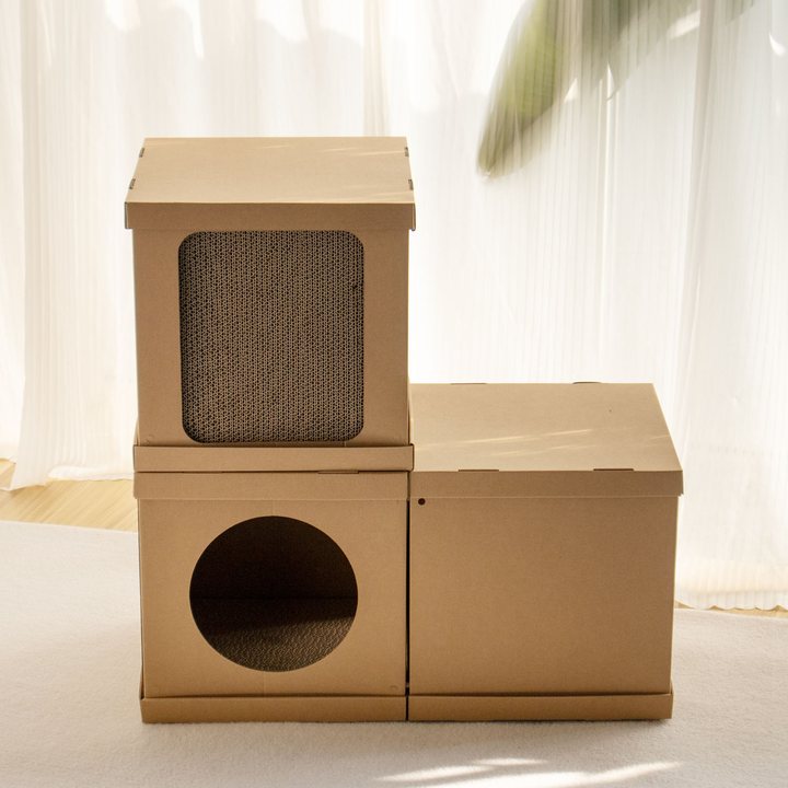 Stacked kraft cardboard cube modules forming a cat house, one cube with a corrugated scratch panel and one with a round doorway