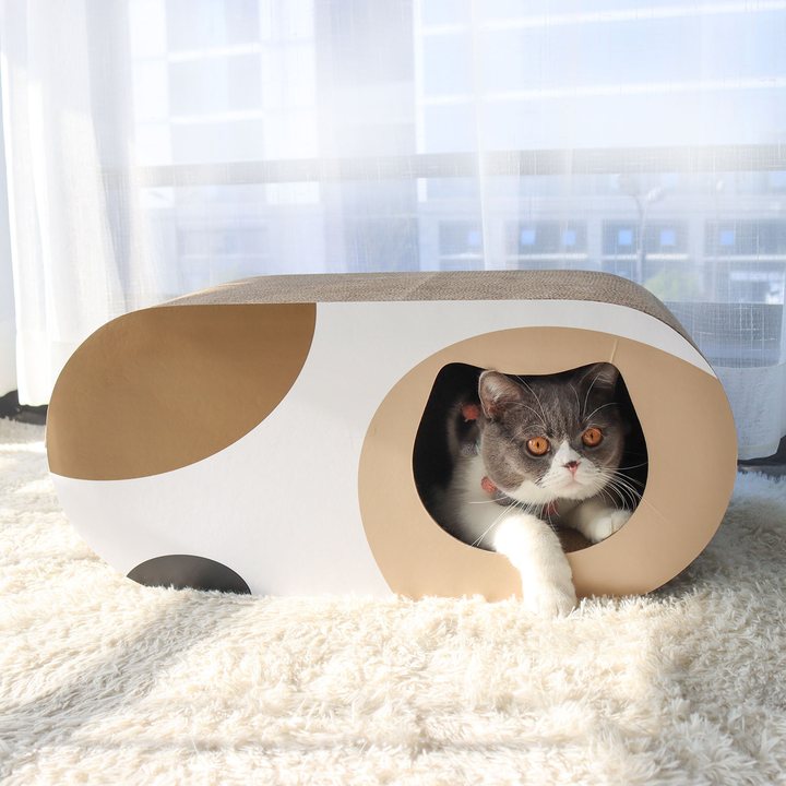 Oval cardboard cat house with a tan and white color-block exterior and a round tunnel entrance