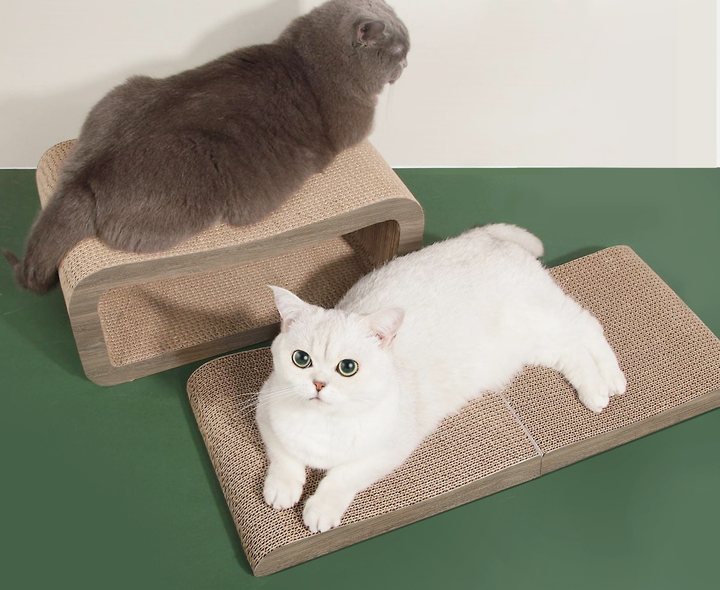 Two-piece cat scratcher set in plain tan corrugated board: a raised arch lounge with a grey cat sitting on it, beside a flat two-section scratch pad with a white cat lying on it.