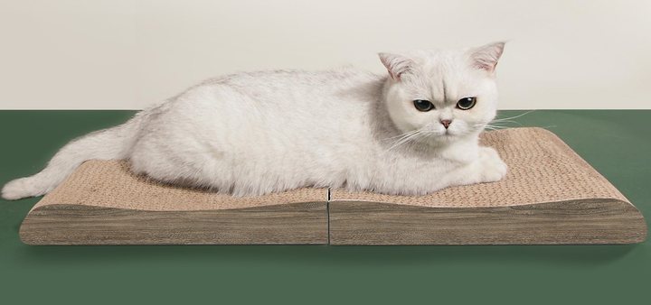 Extended wave-curve cat scratcher lounge with a tan corrugated scratching surface on a dark wood-look base, a white cat lying stretched along its full length.