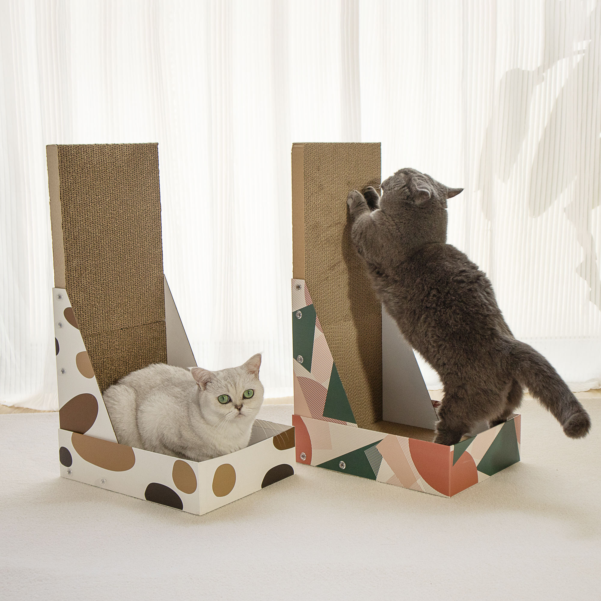 Two L-shaped cat scratchers with enclosed low trays, one brown-spot print and one geometric print; cats are resting and scratching.