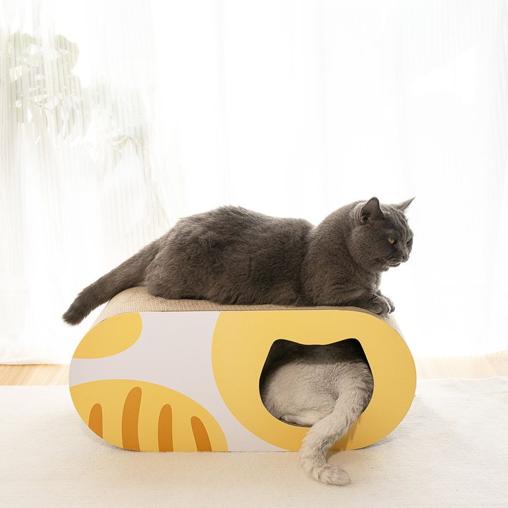 Oval cardboard cat hideaway with a printed pattern, two round entrance holes and a corrugated scratch top.