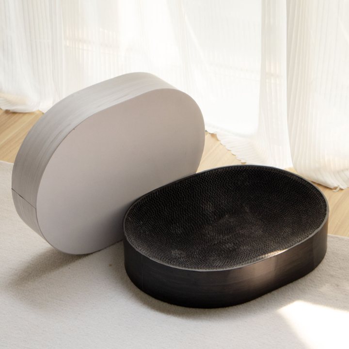 Two oval cat scratcher lounges with a smooth plain outer shell, shown in grey and black finishes.