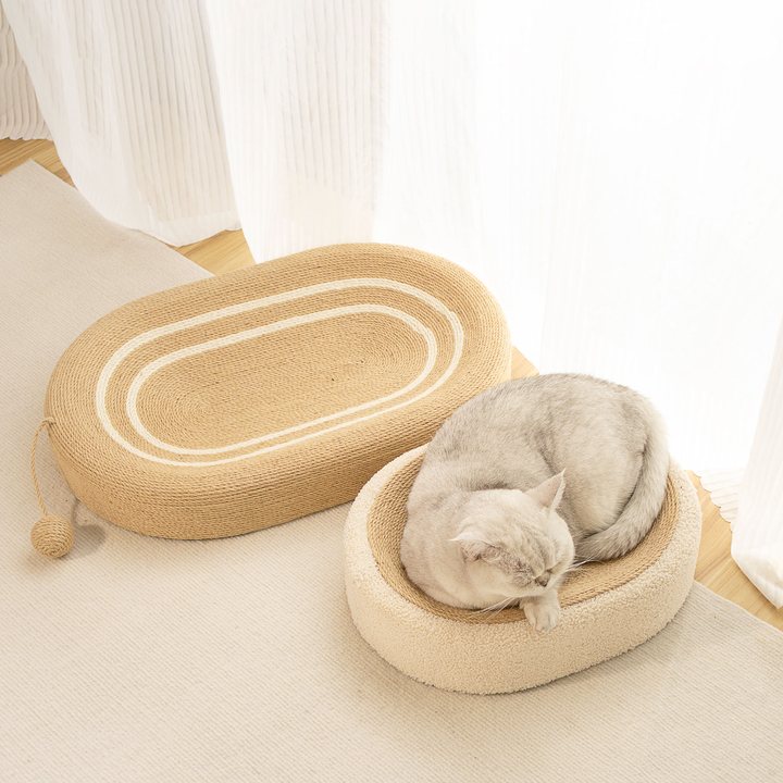 Oval sisal-rope cat scratcher nest shown in a home setting next to a round plush cat bed.