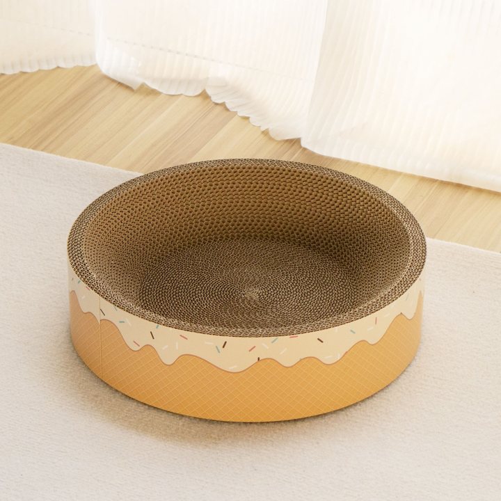 Round cat scratcher nest bowl printed with a donut-icing pattern, shown empty in a home setting.