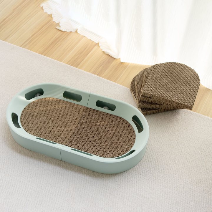 Sage green oval cat scratcher tray with a molded frame and a stack of curved cardboard refill pads beside it