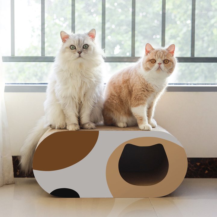 Oval cat house scratcher with a color-blocked brown, tan, cream and black pattern and a cat-face-shaped entry hole