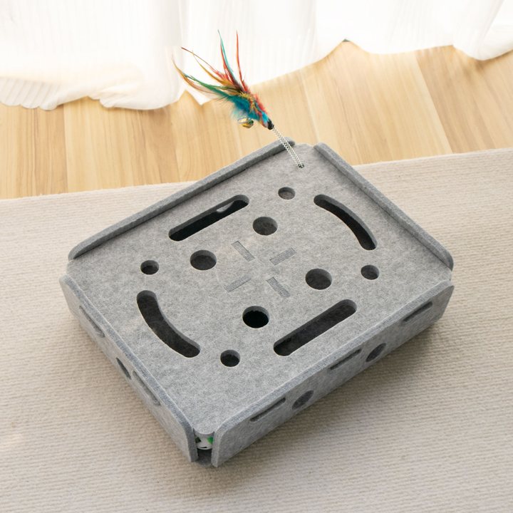 Grey felt cat puzzle box with cut-out holes and an attached feather toy.
