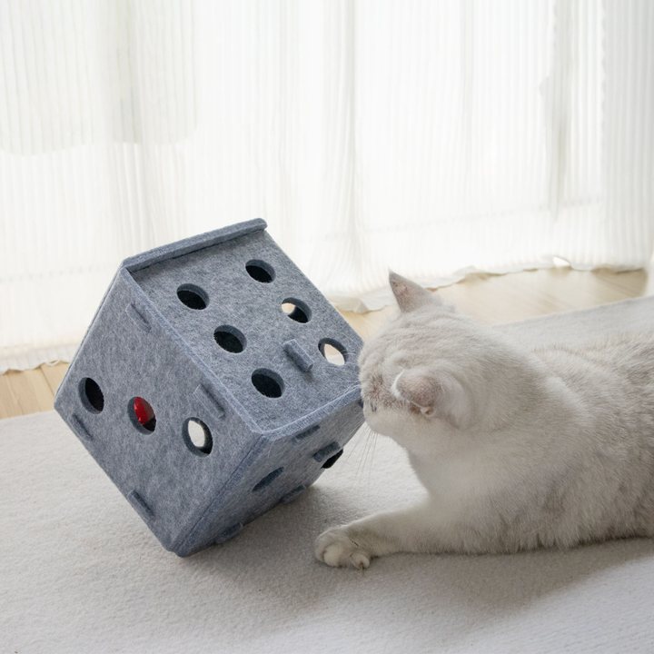 Grey felt dice-shaped cat puzzle box with circular cut-out holes and a ball visible inside one opening.